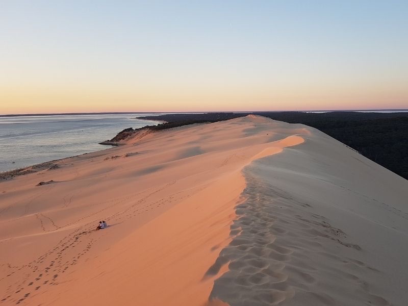 Un couple admirant un coucher de soleil depuis le sommet de la Dune du Pillat en hiver